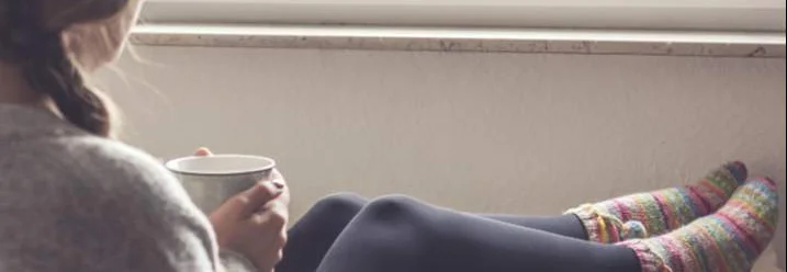 Person sitzt mit Tasse an Heizung